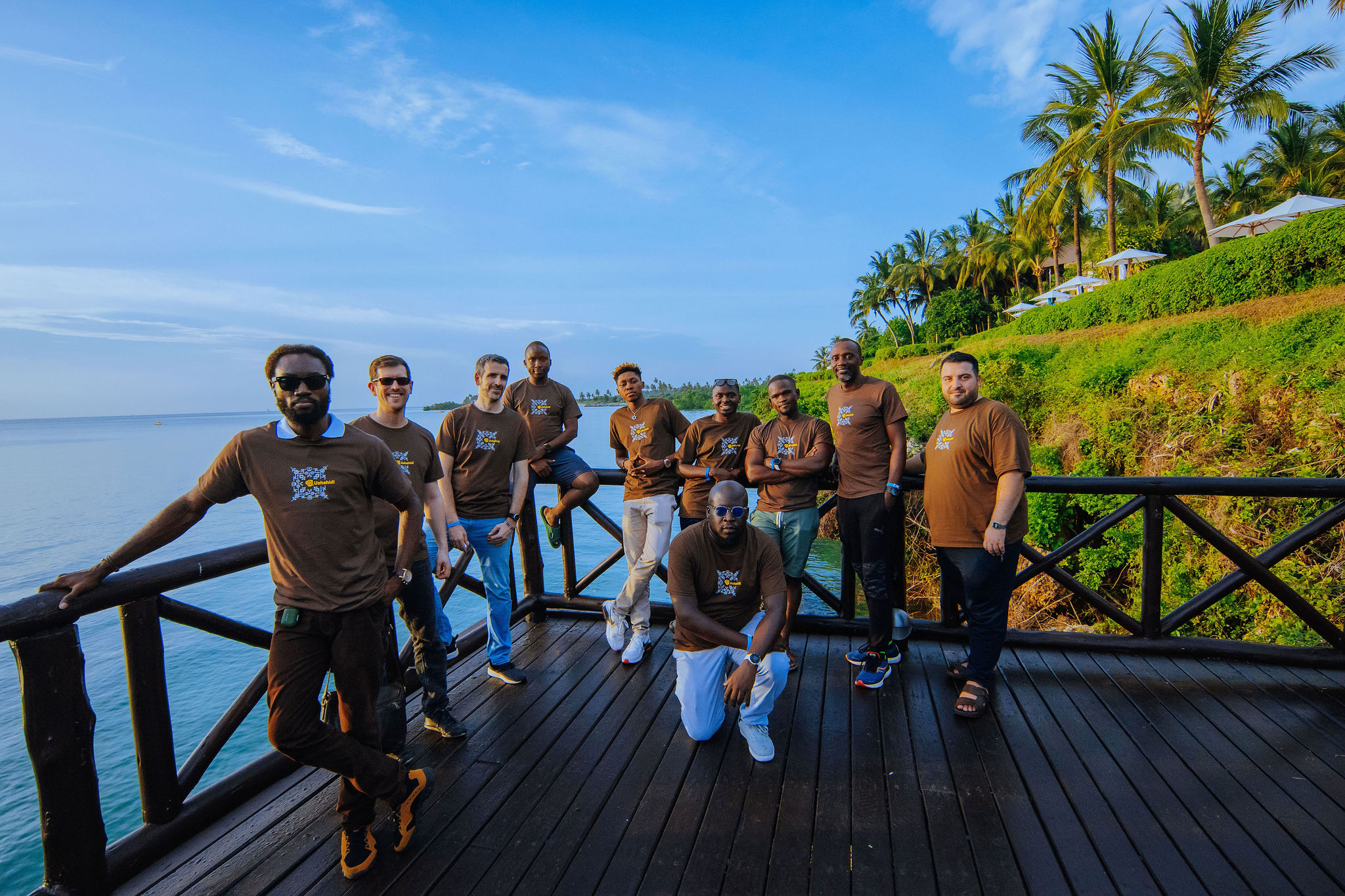 10 men posing for a photo on a deck by the ocean